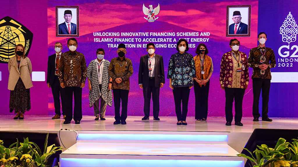 A group of people stand in front of a wall-sized screen displaying the text  'Unlocking Innovative Financing Schemes and Islamic Finance to accelerate a Just Energy Transition in Emerging Economies'.